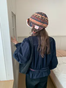 Back view of a woman wearing a warm thick plush Fair Isle trapper hat in a bedroom.