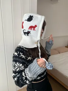 Detail view of a white knitted balaclava with cat patterns and pom-poms on an Asian model