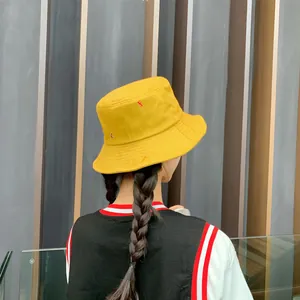 Primer plano de un sombrero de pescador amarillo con bordado rojo en una modelo asiática.