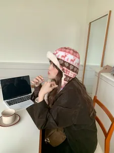 Side profile of a woman wearing a plush pink Fair Isle trapper hat in a cozy indoor setting