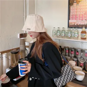 Woman wearing a cream pleated bucket hat and black blazer in a cozy cafe