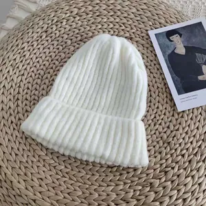 Close-up of a white ribbed knit beanie hat presented on a rustic straw background mat.