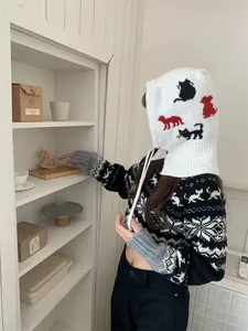 Detail view of a white knitted balaclava hat with colorful cartoon cat patterns worn by a model