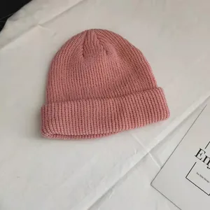 Close-up view of a pink ribbed knitted beanie cap on a white textured fabric background