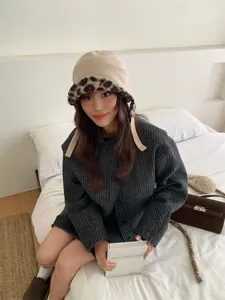 Vrouwelijk model draagt een beige corduroy pilotenmuts met luipaardprint pluche voering in bed