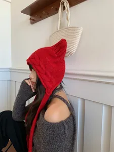 Close-up detail of a cozy red winter knitted beanie with cute cat ears worn by a young woman.