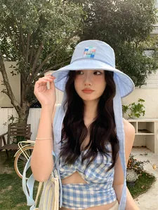 Dettaglio di un cappello da sole a scacchi azzurro con toppa floreale e lunghi lacci