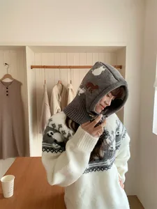 Cozy grey knitted balaclava with cute cat patterns shown on a model in a warm room.