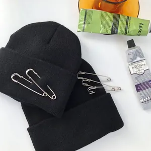 Dettaglio del berretto in maglia nera decorato con spilli di sicurezza argentati.
