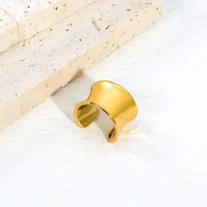 Detail view of a polished gold C-shaped ear cuff resting on a textured stone background