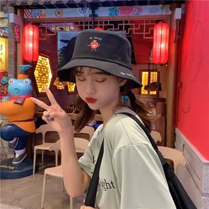 Detailed view of a black bucket hat with a cute tomato embroidery worn by a model.