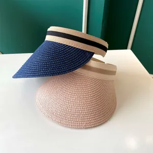 Détail macro de visières de soleil en paille marine et rose avec bandeau rayé.