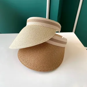 Gros plan de visières en paille beige et marron avec bandes rayées sur une surface blanche