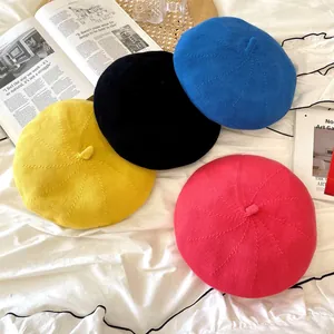 Detailed view of four colorful knitted beret hats for women on a cozy white bedsheet