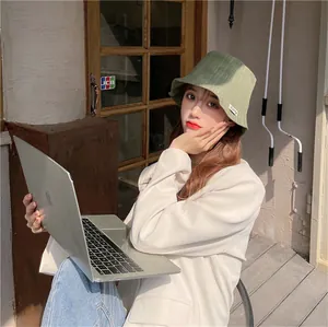 Stylish Asian woman wearing a green pleated bucket hat while holding a laptop outdoors