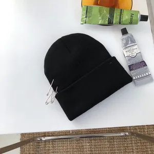 Vista dall'alto di un berretto nero a maglia alla moda con spille da balia argento.