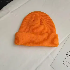 Detailed close-up view of a vibrant orange ribbed knit beanie on a clean white fabric background