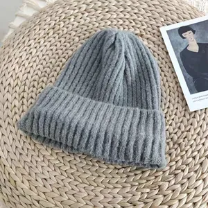 Macro detail of a grey ribbed knit beanie hat lying on a natural woven straw mat.