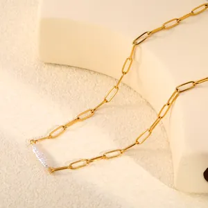 Gros plan d'un collier chaîne trombone doré avec une perle baroque blanche au design minimaliste