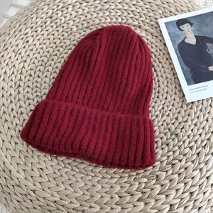 Detailed view of a dark red ribbed knit beanie placed on a woven straw background mat.