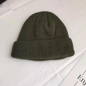 Macro detail of dark green short knitted beanie hat with rib texture on white cloth