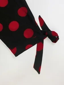 Détail d'une robe noire à gros pois rouges avec une ceinture à nouer à la taille.