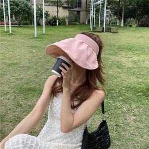 Stilvolle Frau mit einem rosa Sonnenvisier mit breiter Krempe in einem sonnigen Park