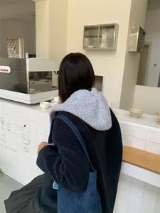 Back view of a cozy light blue knitted hood and scarf combo shown in a cafe setting.