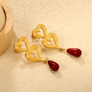 Macro view of textured double heart earrings featuring a deep red teardrop faux pearl pendant.