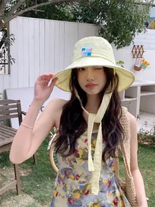 Dettaglio di un cappello da sole a scacchi gialli con laccetto indossato in giardino