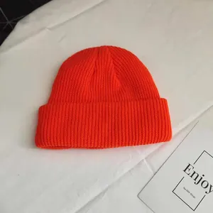 Close-up detail of a bright orange short ribbed knit beanie hat showing woven texture