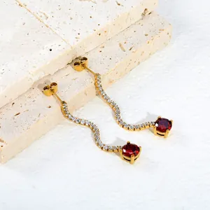 Detail van gouden kwastjes oorbellen met een groot rood kristal en zirkonia-accenten.