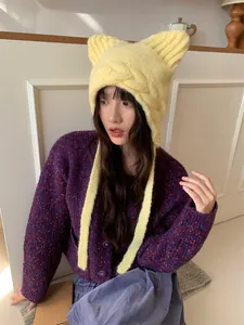 Detail view of a model wearing a cute yellow cat ear knitted beanie hat with tassels