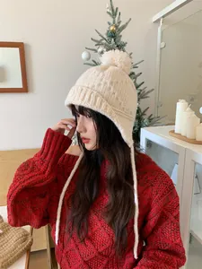 Vista lateral de gorro de punto beige con orejeras y pompón para mujer en invierno