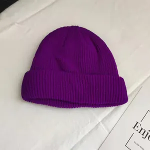 Detail view of a vibrant purple ribbed knit beanie hat on a white surface