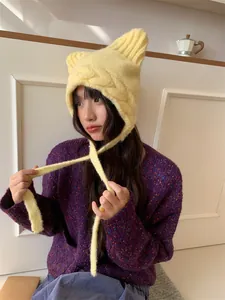 Detailed view of yellow cat-ear knitted hat with long straps worn by a model in lifestyle shot