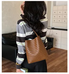 Vista trasera de una modelo con un bolso cubo trenzado marrón en un ambiente acogedor.