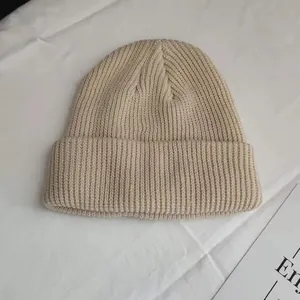 Close-up detail of a minimalist beige knitted beanie hat featuring classic ribbed texture