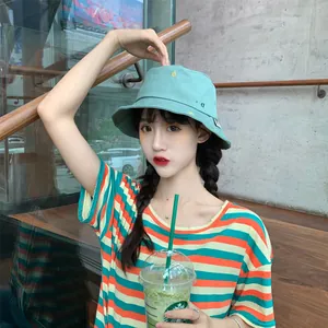 Primer plano de una mujer joven con un sombrero de pescador bordado verde menta en un entorno