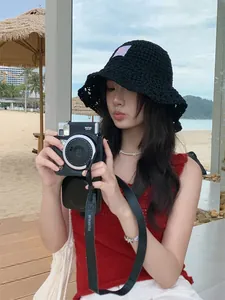Modelo asiática con un sombrero de pescador de ganchillo negro y cámara en la playa