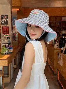 Close-up of blue checkered wide-brim bucket hat with pink trim and chin strap on model.