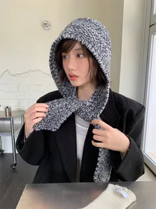 Close-up of a grey knitted hooded scarf balaclava worn by a model in a cozy indoor setting.