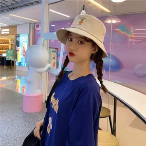 Detailed view of a beige bucket hat with cute carrot embroidery worn by a model.