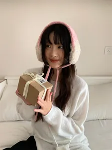 Mannequin asiatique portant des cache-oreilles en peluche rose et beige avec un cadeau.