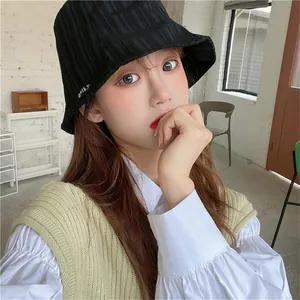 Young woman wearing a black pleated bucket hat for stylish summer sun protection indoors