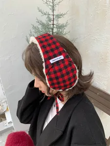 Red and black plaid plush earmuffs with lace-up chin strap worn by a model