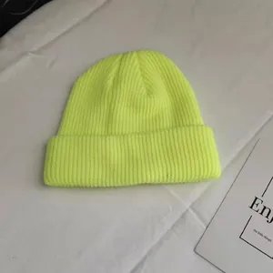 Detail view of a vibrant neon yellow rib-knit beanie hat on white fabric surface