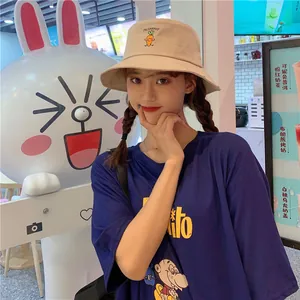 Cute beige bucket hat with carrot embroidery worn by a young woman in a trendy cafe