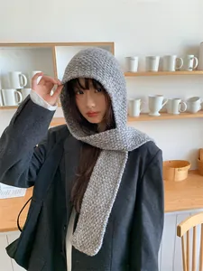 Detailed view of grey knitted hood scarf worn by a model in a cozy cafe setting.