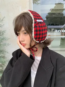 Close-up view of a woman wearing red and black checkered plush earmuffs with ties